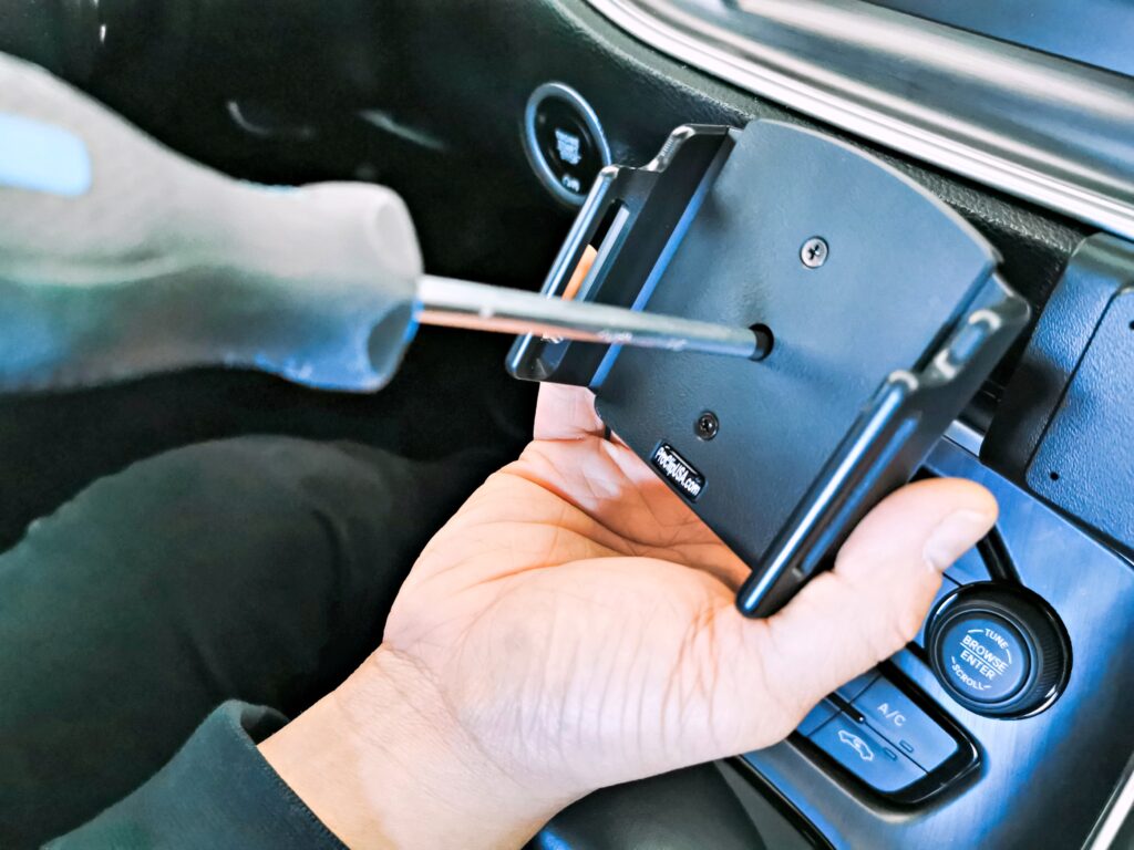 A Philips screwdriver is loosening a screw in the center of phone holder. 