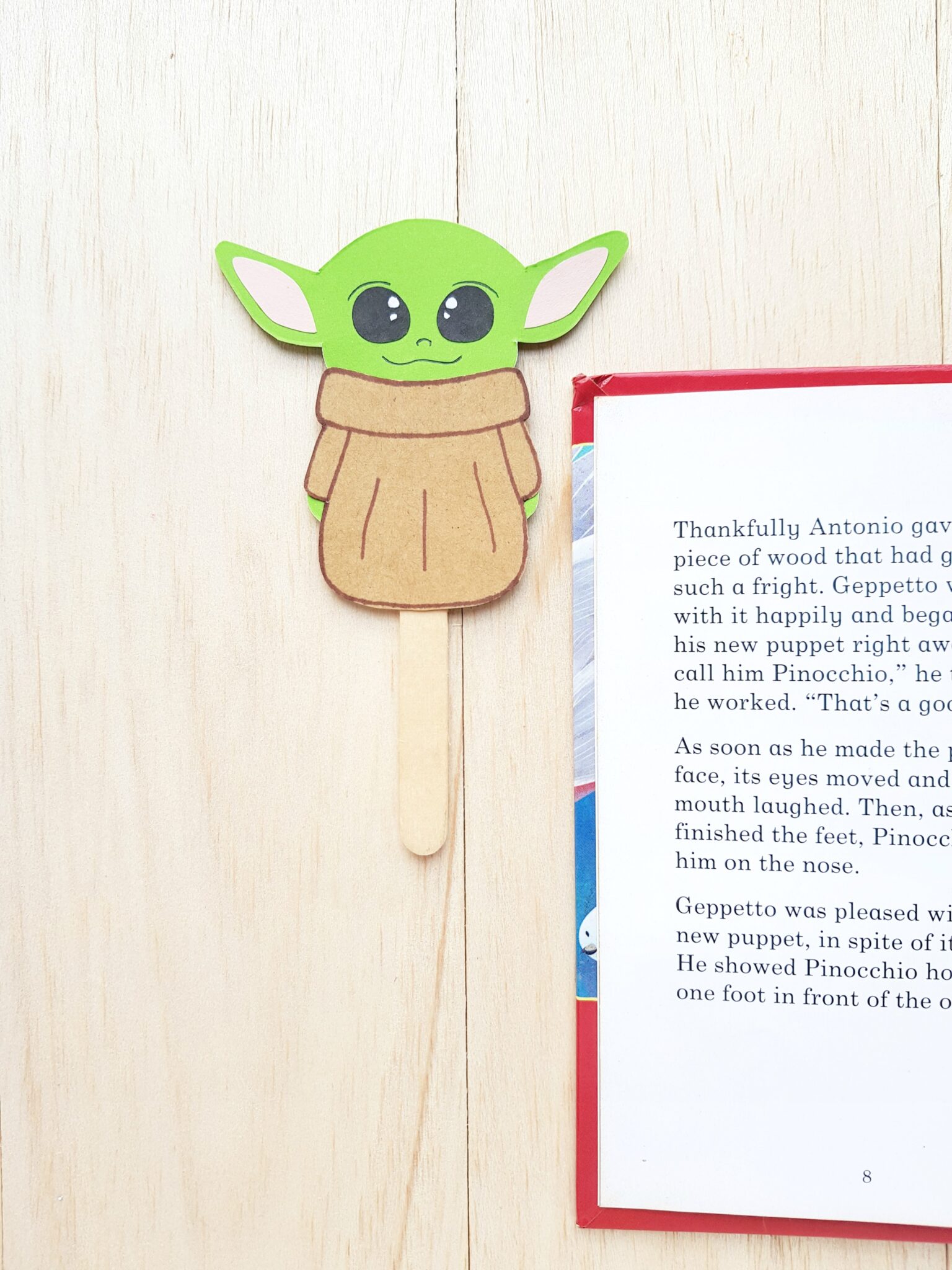 A super cute Baby Yoda paper craft turned into a bookmark. Bookmark is next to an open book. 