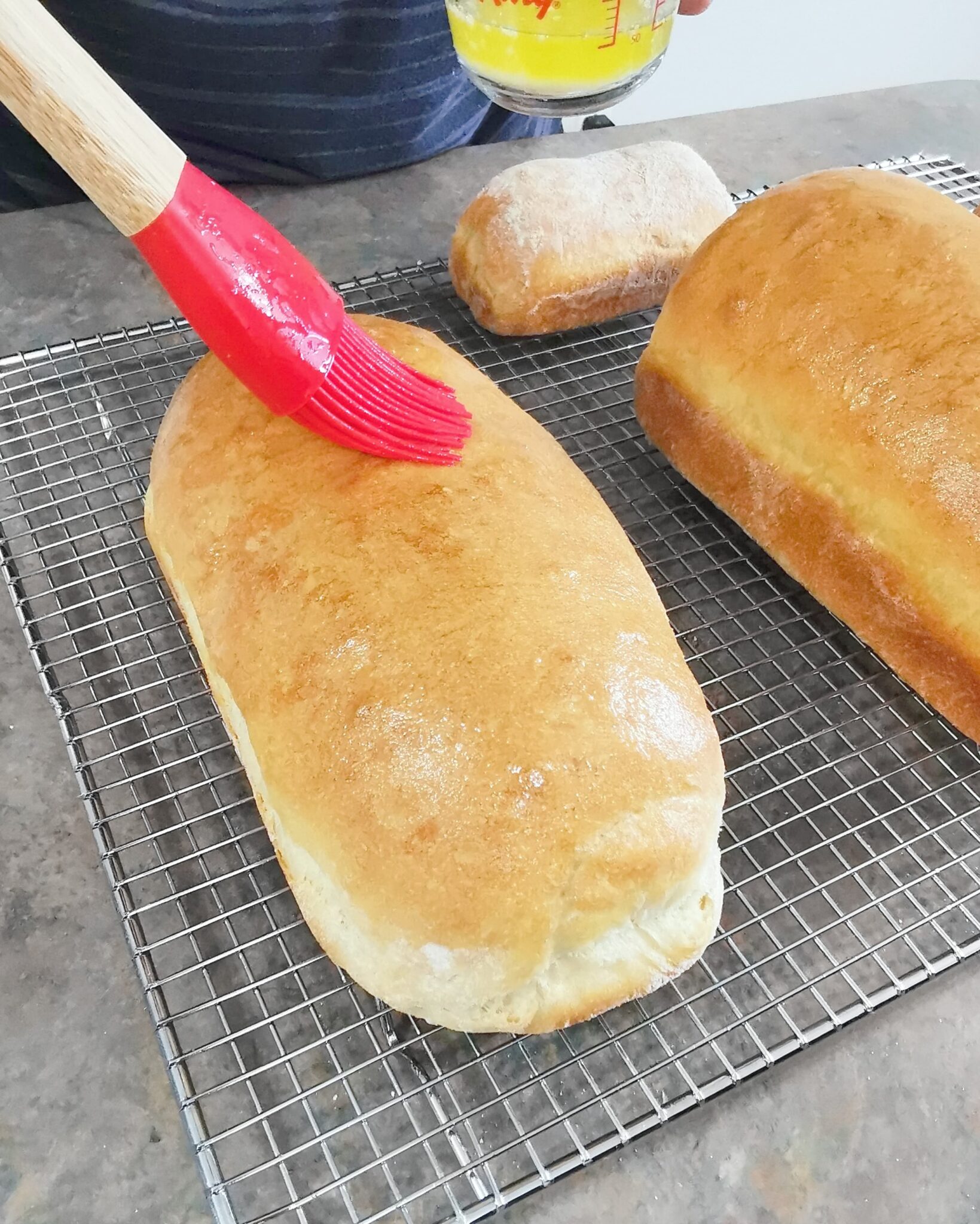 Bread loaves being buttered with a brush. 