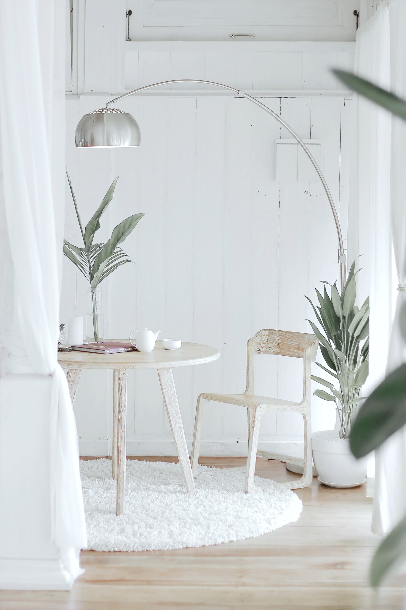 A white room with a table and chair, acting as a home office. There is a lamp that hangs over it. 