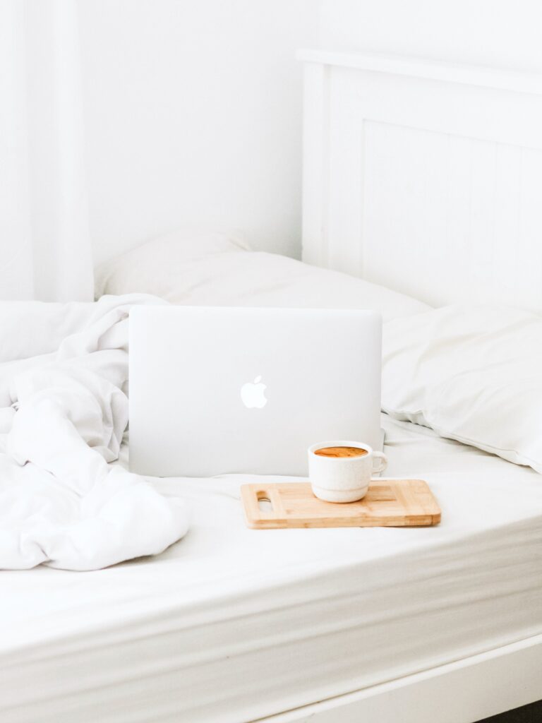 A white bedroom, with white sheets, an Apple laptop with a tray with coffee.