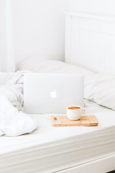 A white bedroom, with white sheets, an Apple laptop with a tray with coffee.