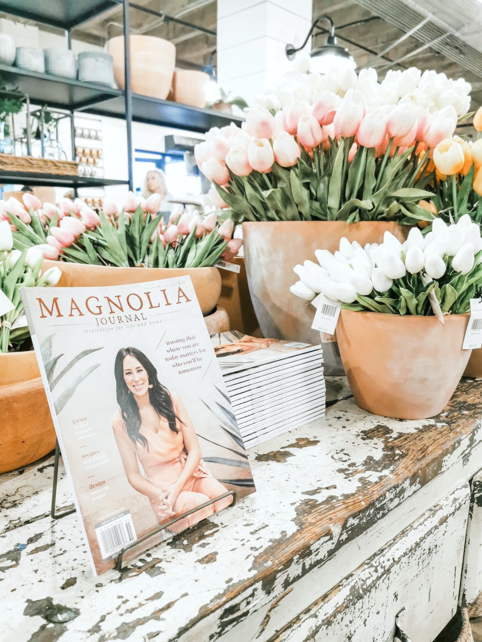 A Magnolia Market magazine on a rustic table with tulips. 