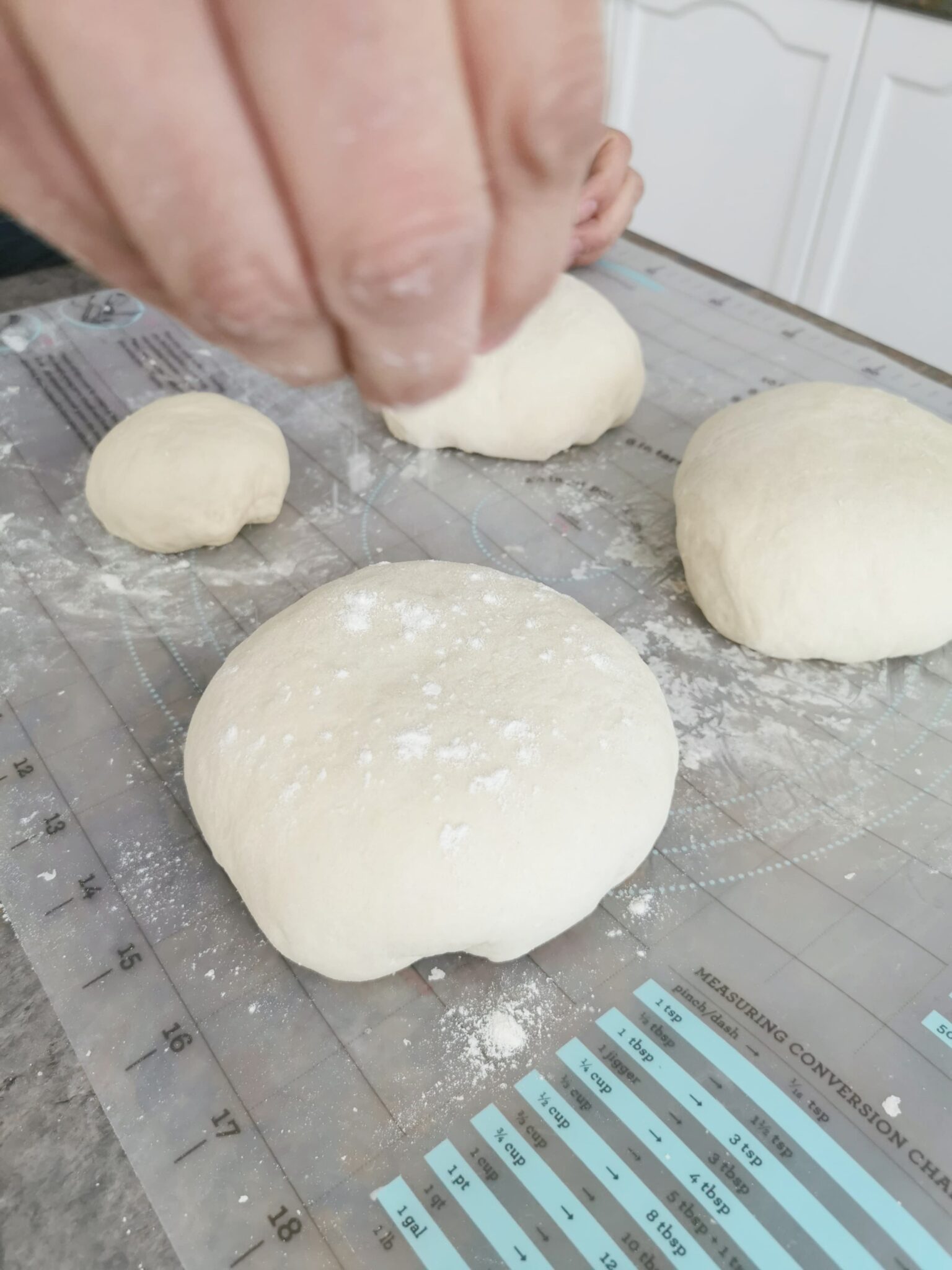 Separated dough into balls, a hand sprinkles dough on each ball. 
