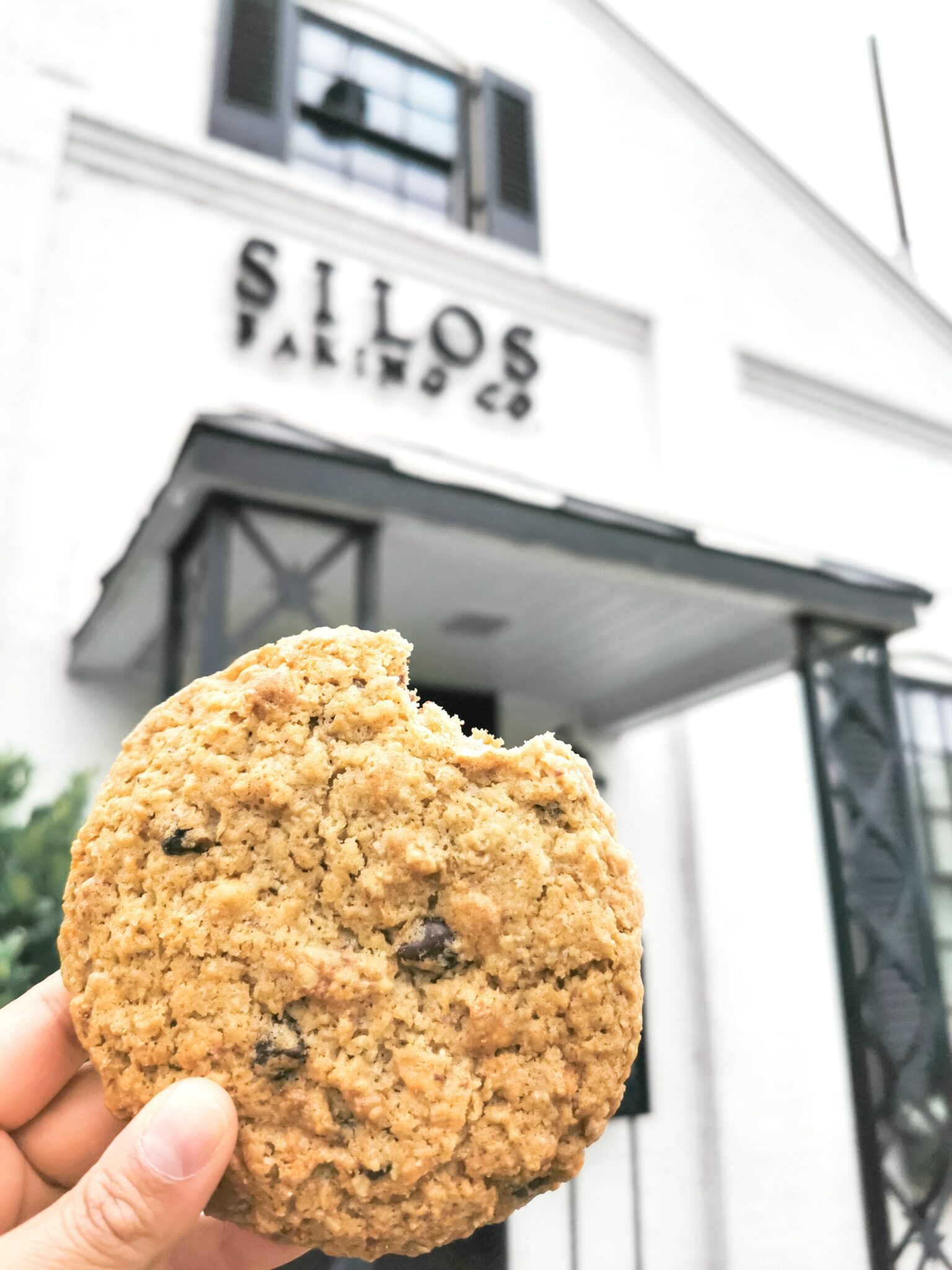 The front entrance of Silos Baking Co. and Nancy's hand while she holds up the Silo Cookie.