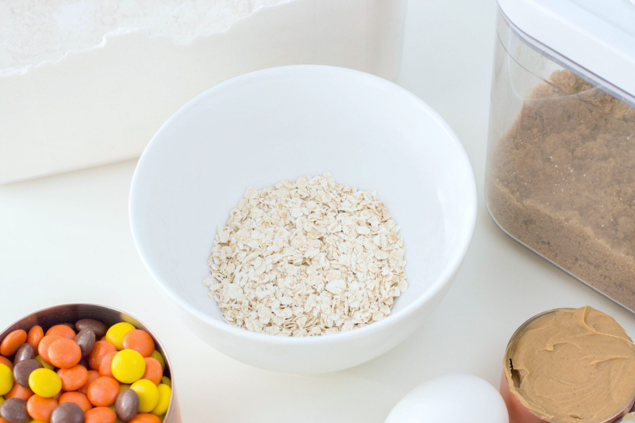 A bowl of oats, peanut butter, eggs, brown sugar, Reese's Pieces, and flour are shown.
