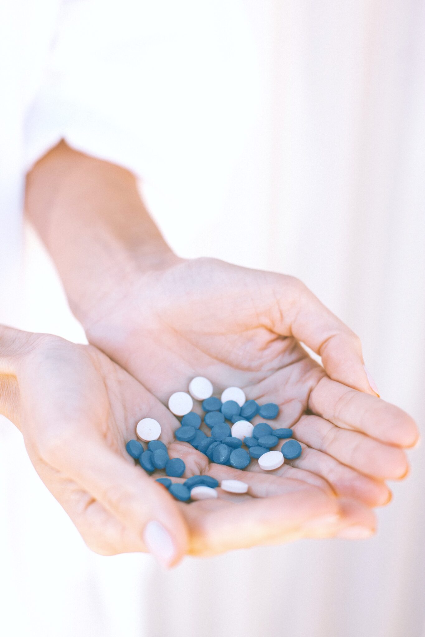 A woman's hand are shown holding handfuls of blue vitamins.