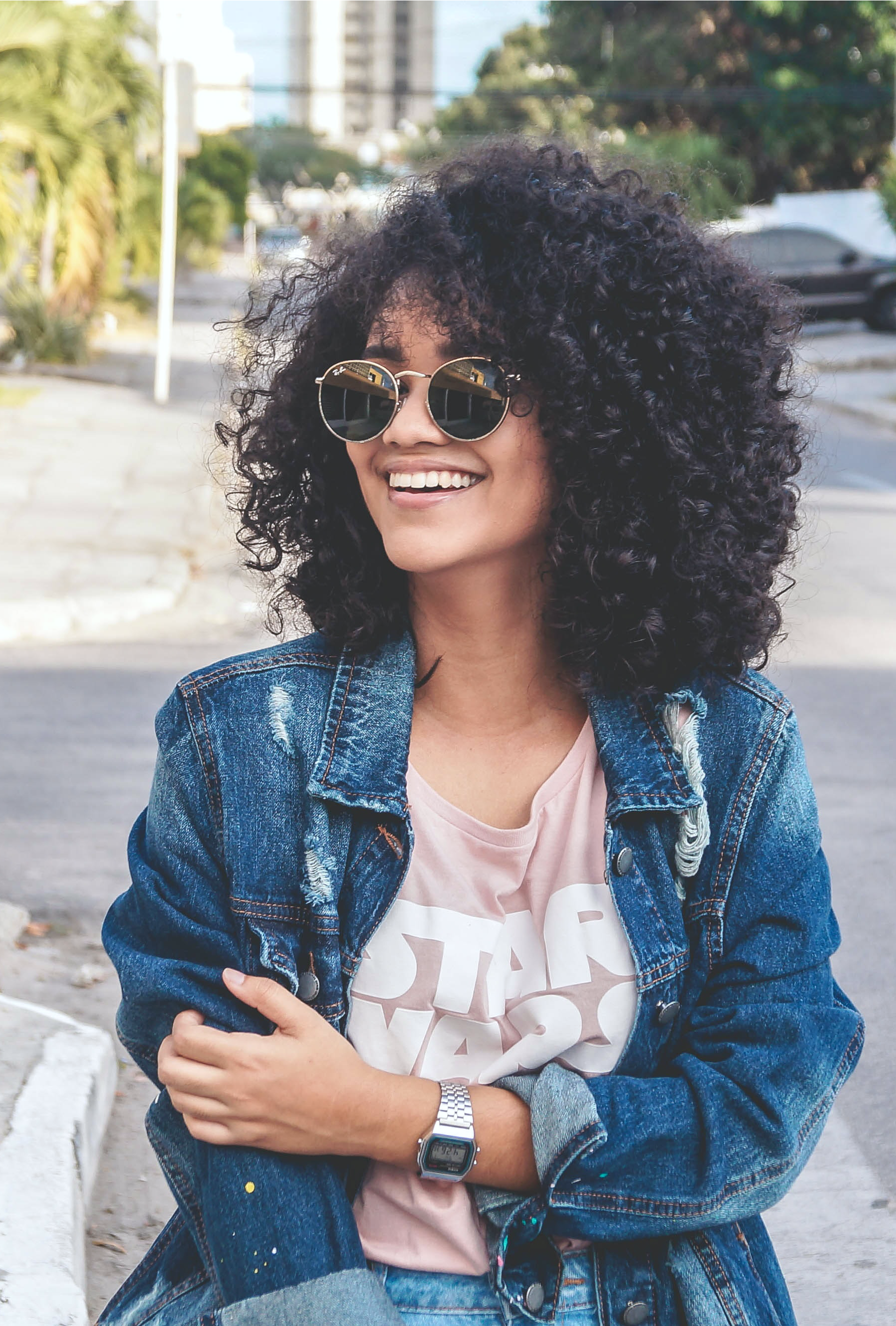 A beautiful black woman smiles and looks away from the camera. She is wearing glasses and has beautiful curls. 