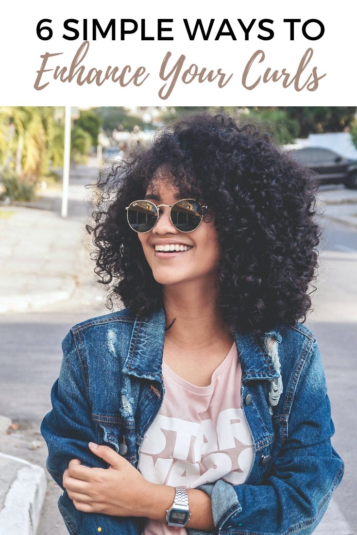 A beautiful black woman smiles and looks away from the camera. She is wearing glasses and has beautiful curls. 