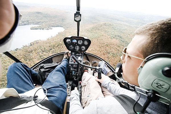 Two men fly a helicopter over wooded area. 