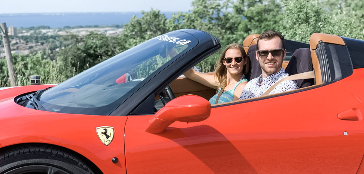 A man and a woman drive an exotic car, a red Ferrari.