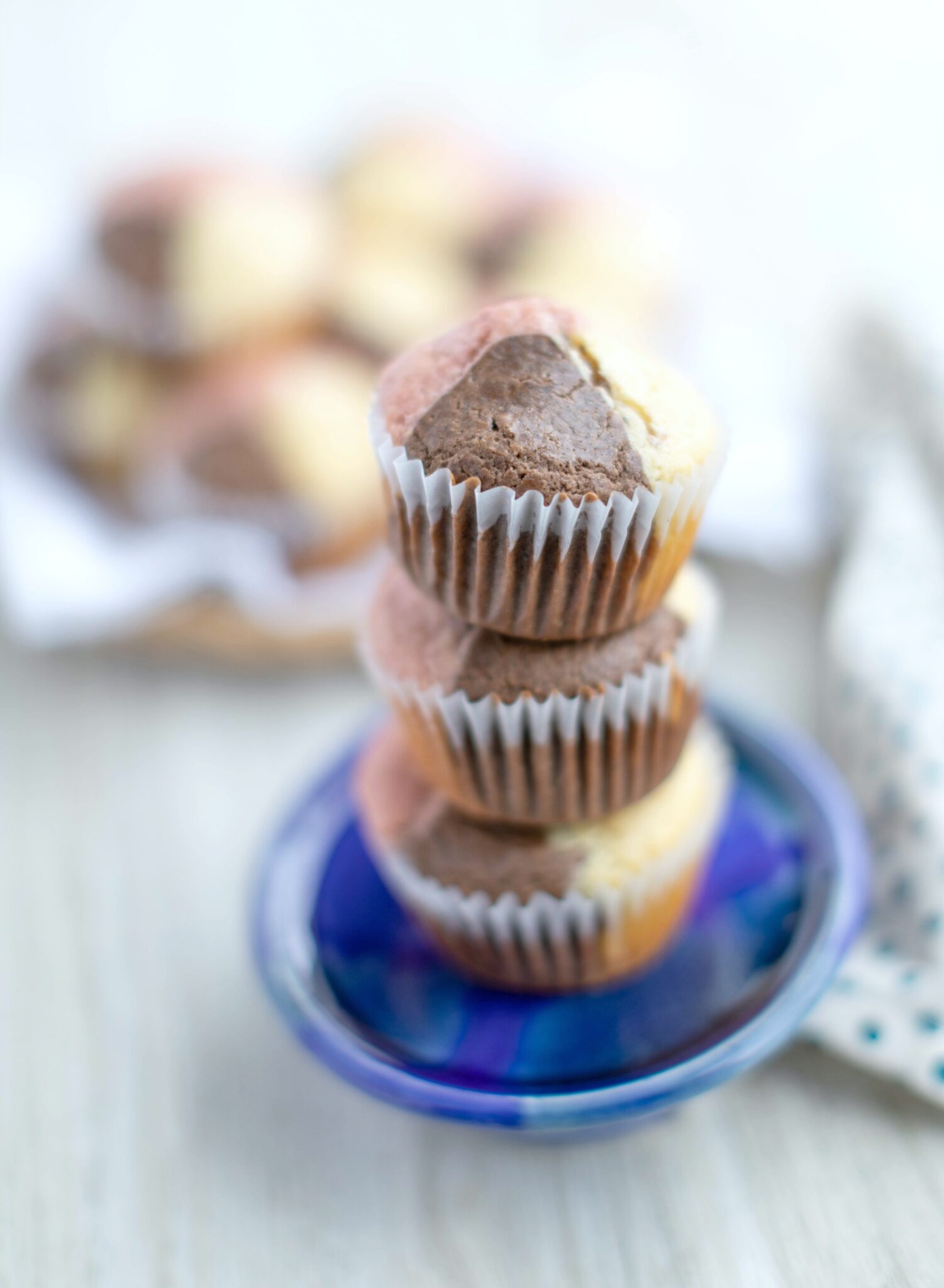 A stack of 3 Neapolitan Ice Cream muffins are on a navy blue dish.  Behind it, you can see a whole plate of muffins.