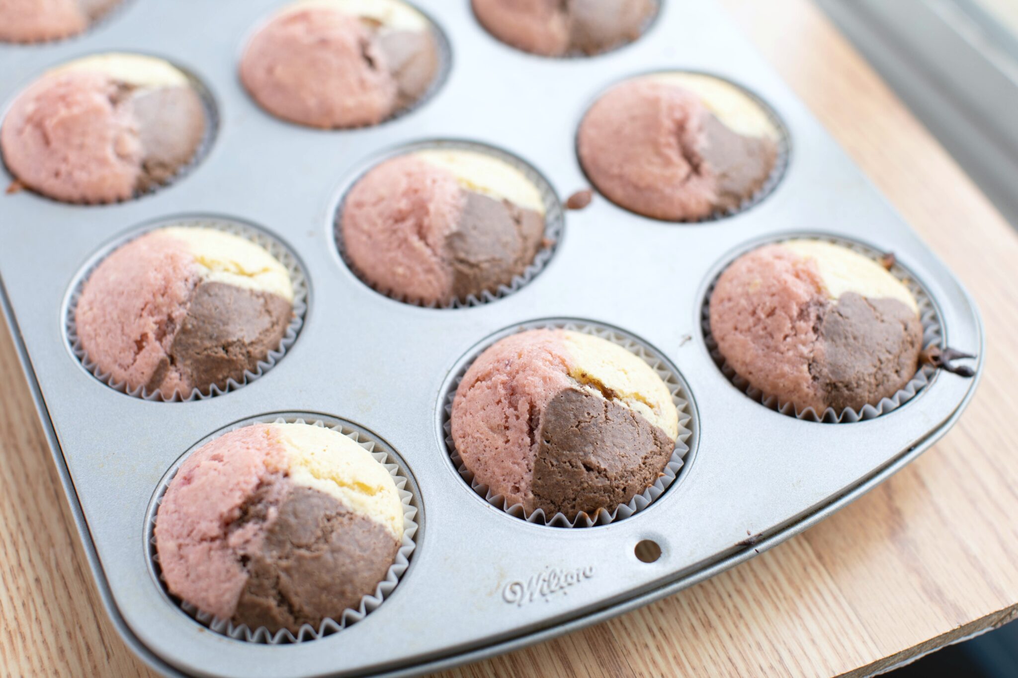 A muffin tray straight out of the oven filled with Neapolitan Ice Cream muffins.