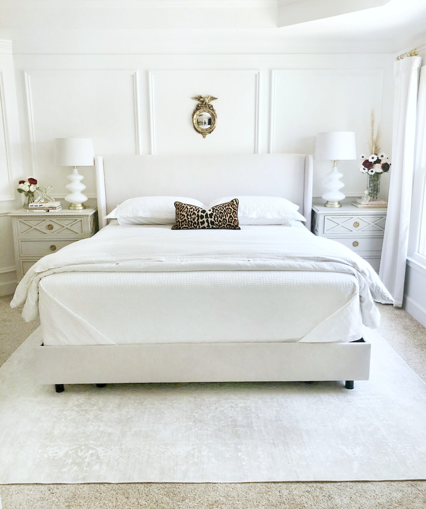 A beautiful, clean, white bedroom, that is tidy. It has a small mirror above the bed. The bedroom is to signify and share the 5 things you should have in your room to keep it tidy.