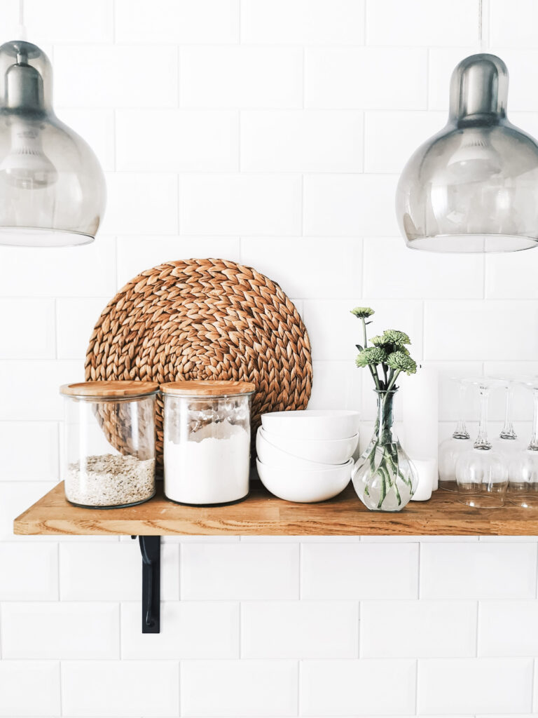 A beautiful farmhouse kitchen shelf with canisters, a plant, and a wicker plate.