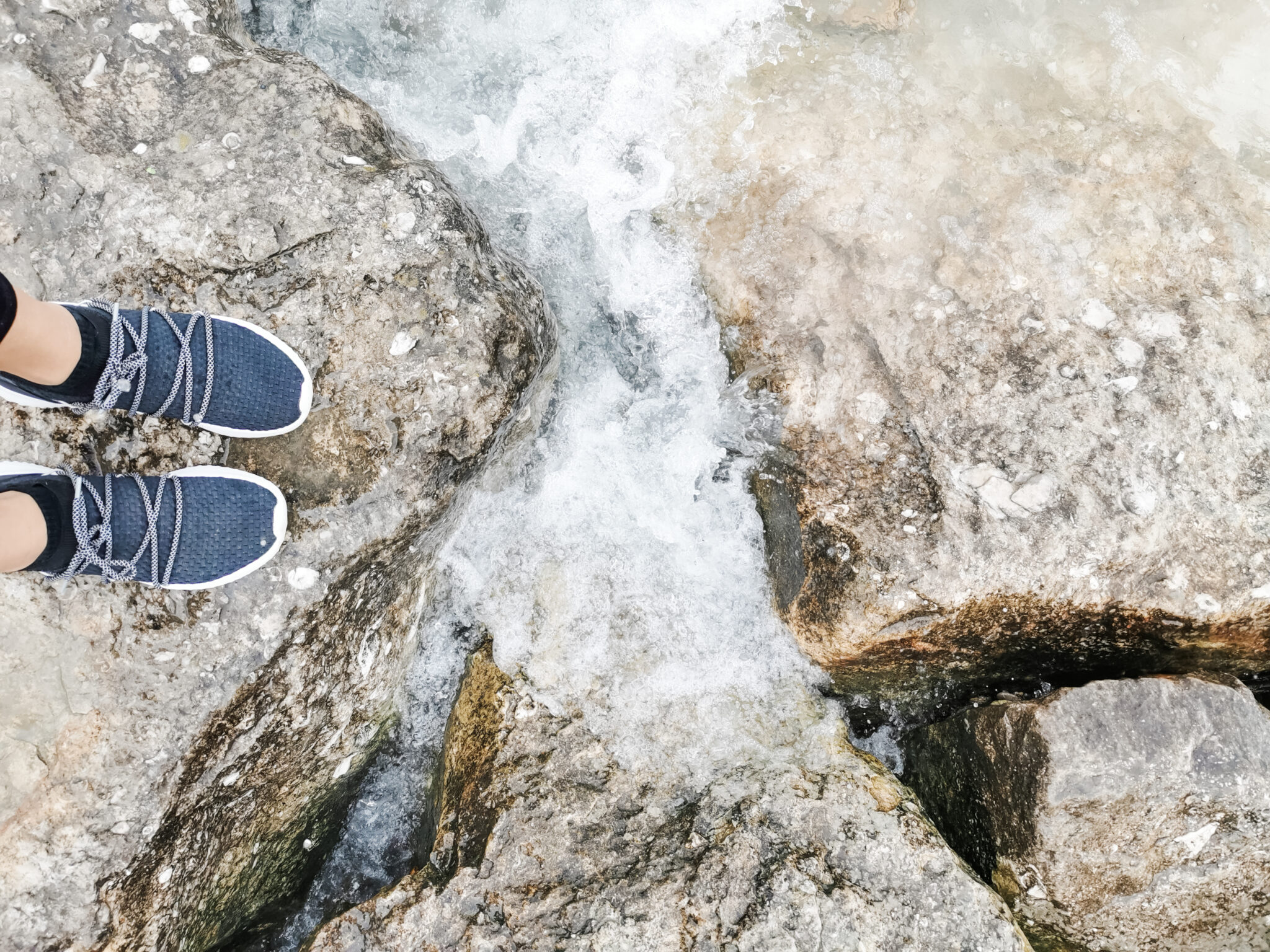 Nancy's feet on top of rocks in Bright's Grove. The waves are crashing into the rocks. 