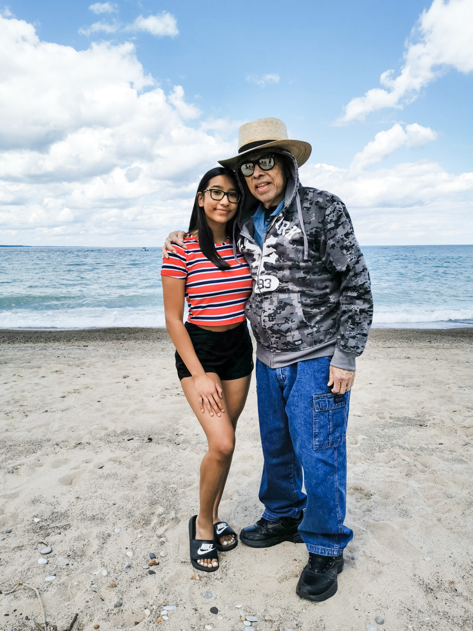 Gabby and her Abuelito posing ont he beach, they are both smiling. 