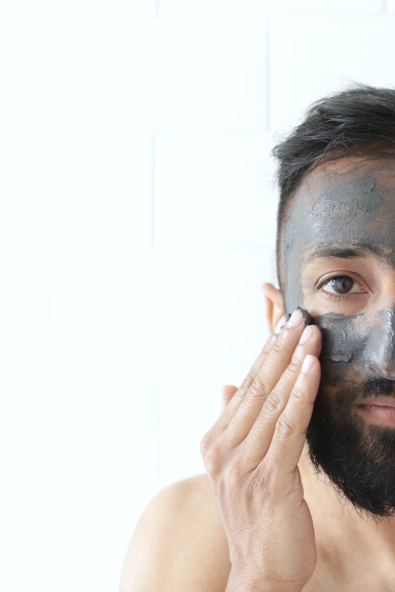 Man puts clay mask on his face and looks straight ahead.