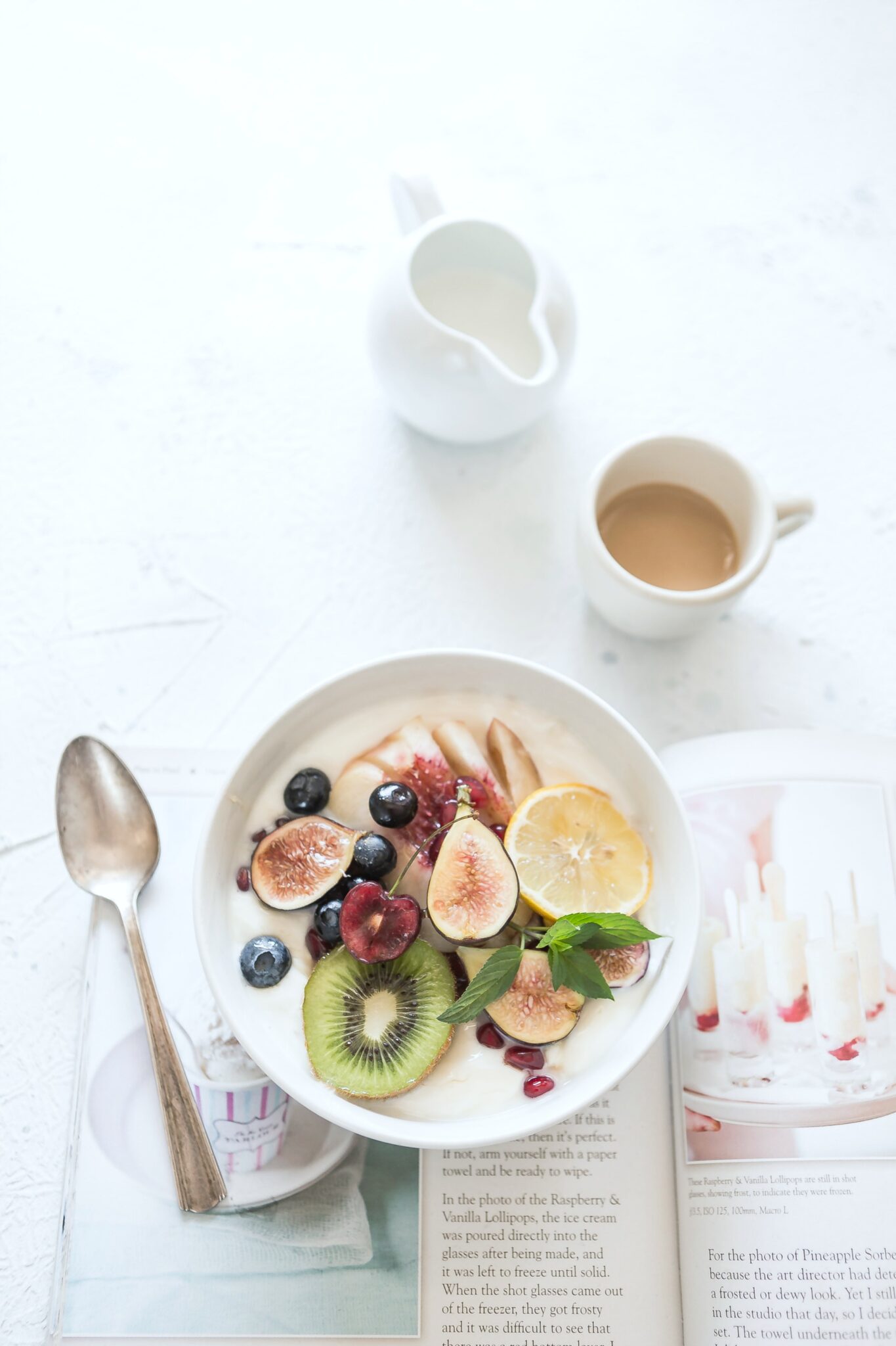 A healthy breakfast of a bowl with fruit and milk. There's a cup of coffee and a good book.