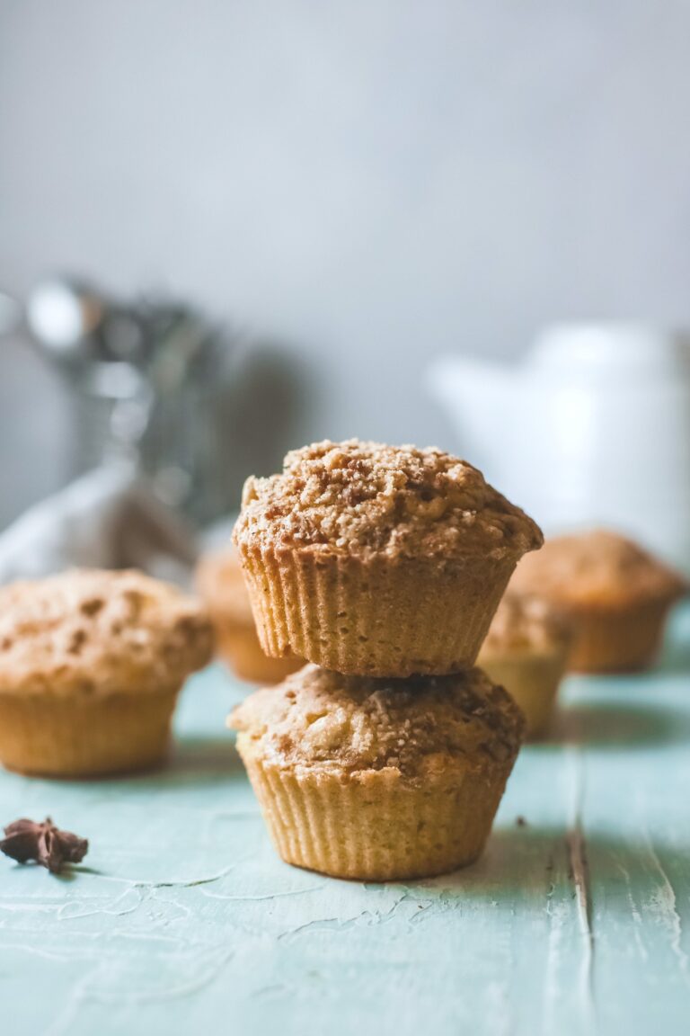 A stack of two pumpkin streusel muffins with more behind it. A tea pot and kitchen towel is seen.