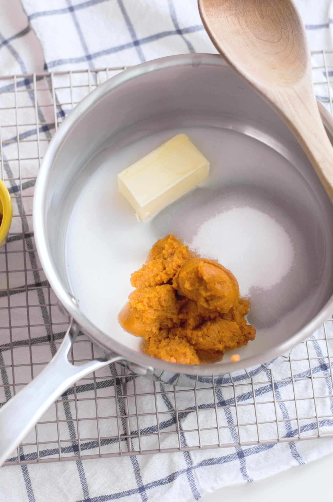 Ingredients in saucepan, sugar, butter, pumpkin puree, and more. A wooden spoon sits on top.