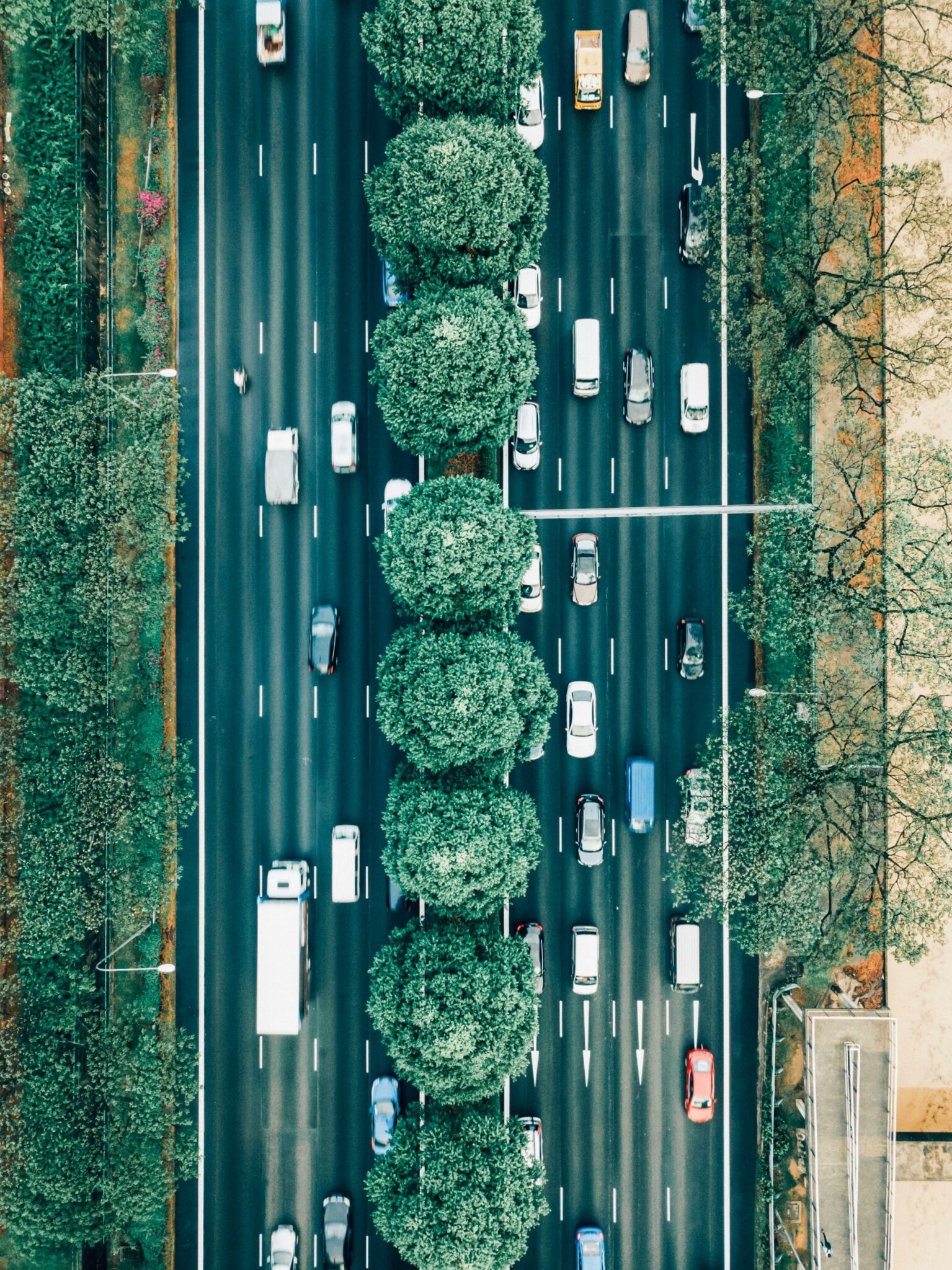 A birds eye view of 4-lane street with traffic going both ways. A tree line separates them.