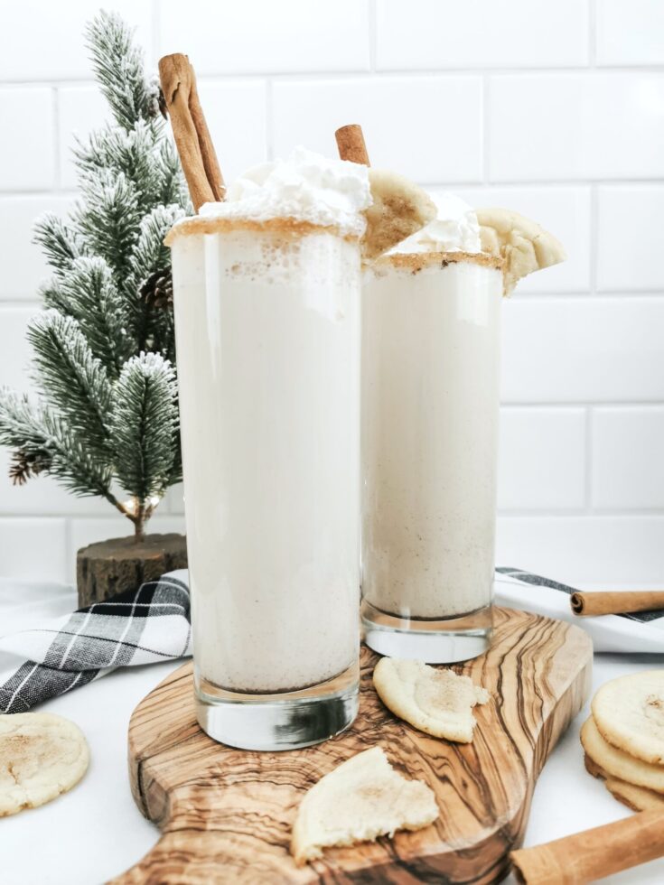 Two Caramel Snickerdoodle mocktails on a board. There's a small Christmas tree in the back and snickerdoodle cookies surround the glasses.