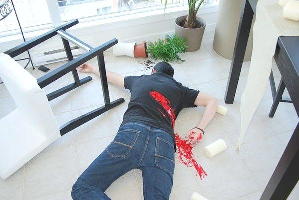 A mock murder scene is shown with a man lying on his stomach with fake blood on his back. A great way to enjoy socially-distanced experiences at home.