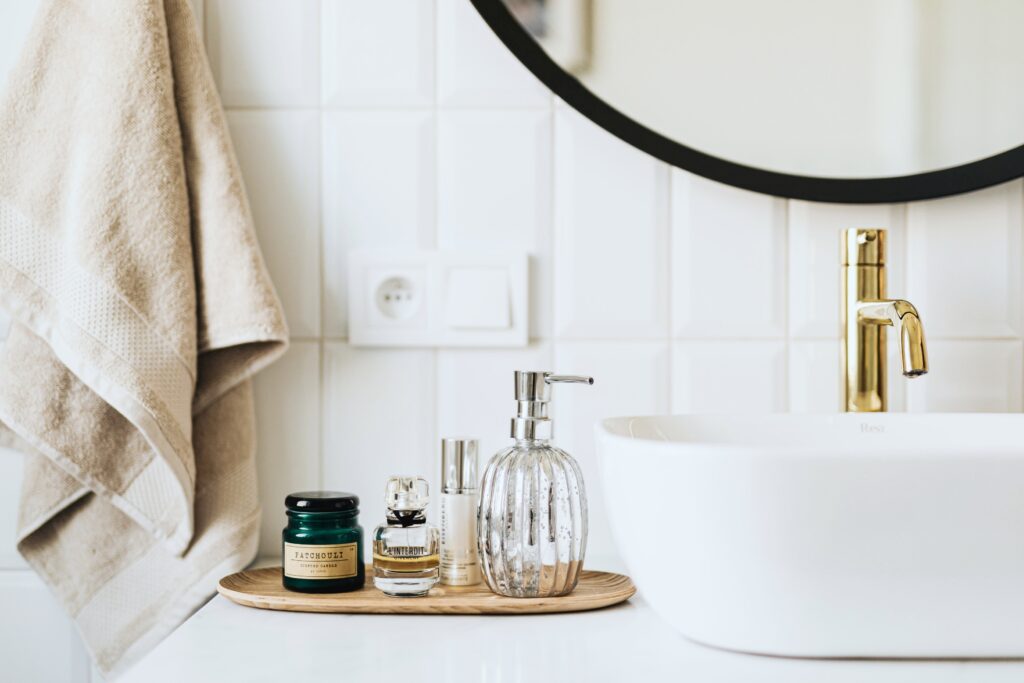 A modern yet rustic bathroom. A white tray with a gold faucet and a tray full with toiletries. Above it is a black round mirror. This article is about ways to spruce up your bathroom.