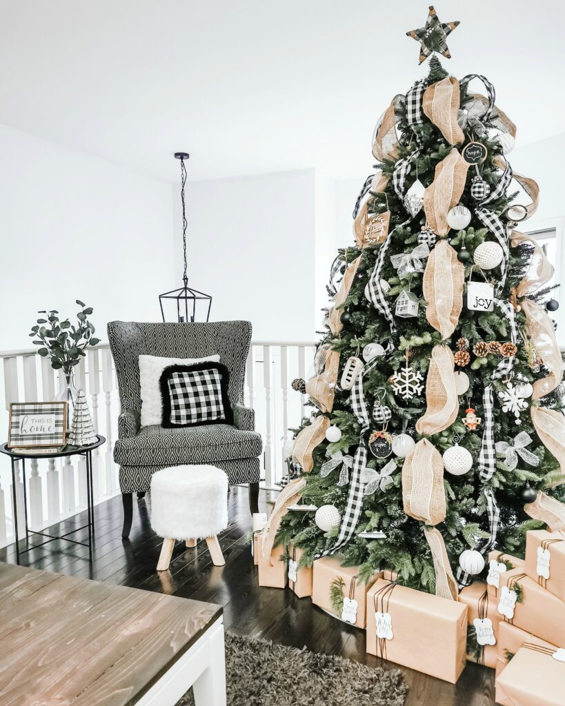A farmhouse style tree with gifts surrounding it. It is placed in a living room with a wing back chair.
