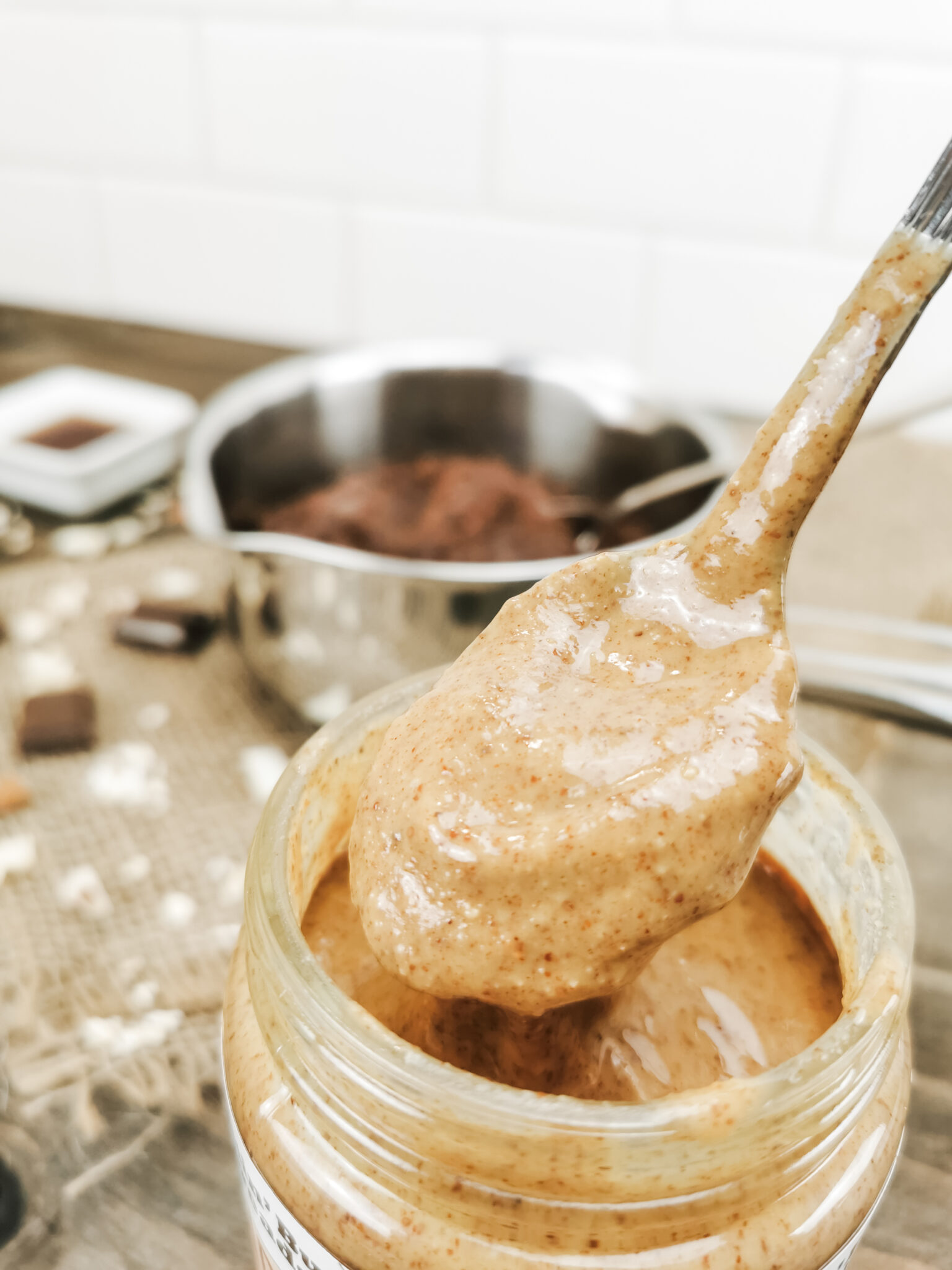 A spoon is being lifted out of almond butter. It is being used to drizzle onto oatmeal.
