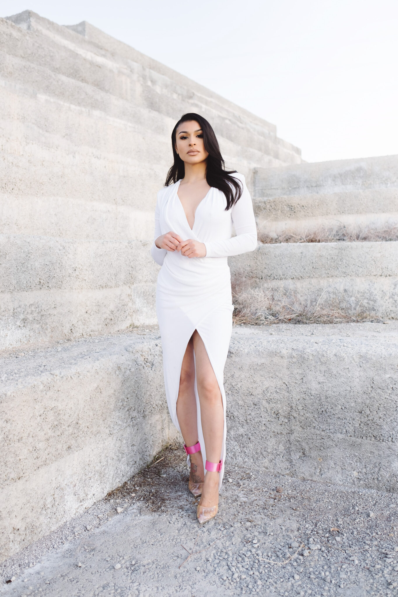 Woman stands in front of a concrete wall wearing a white formal dress. This article explains how to choose a formal dress for your body type.