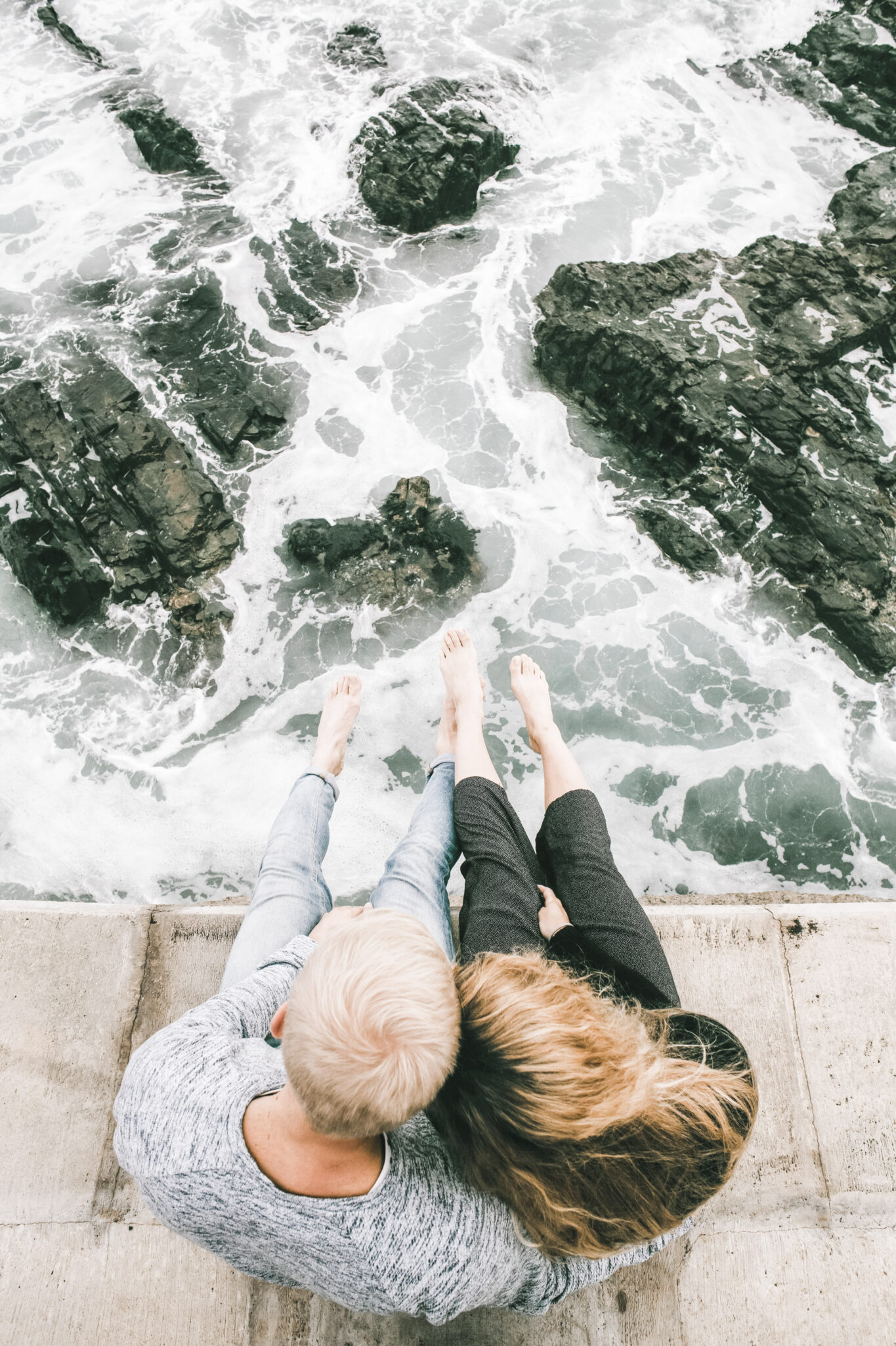 A couple sit together on a ledge and look out to waves crashing below. This article covers 4 things you should take seriously this year.