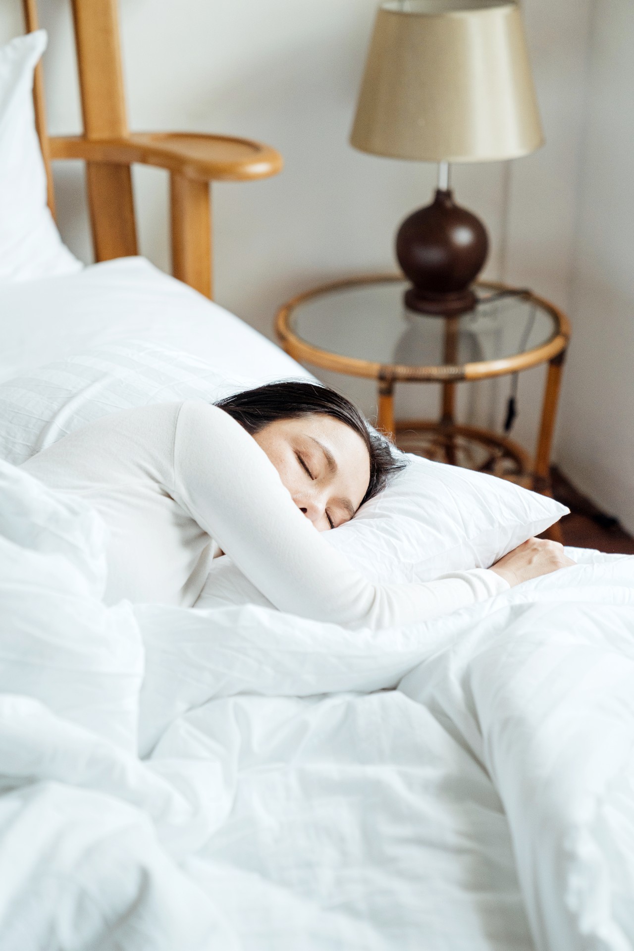 A woman sleeps in a bright room. This article covers 7 bedroom essentials for optimal sleep. 