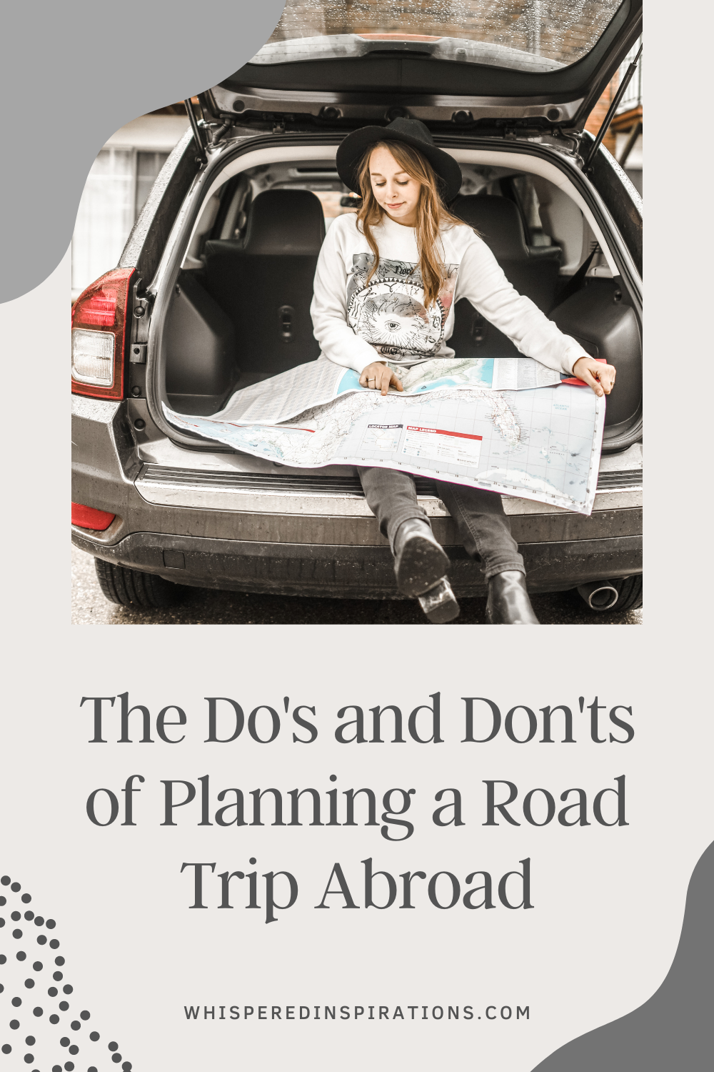 A girl sits in the back of her car holding and reading a map for a road trip. This article covers the do's and don'ts of planning a road trip abroad.