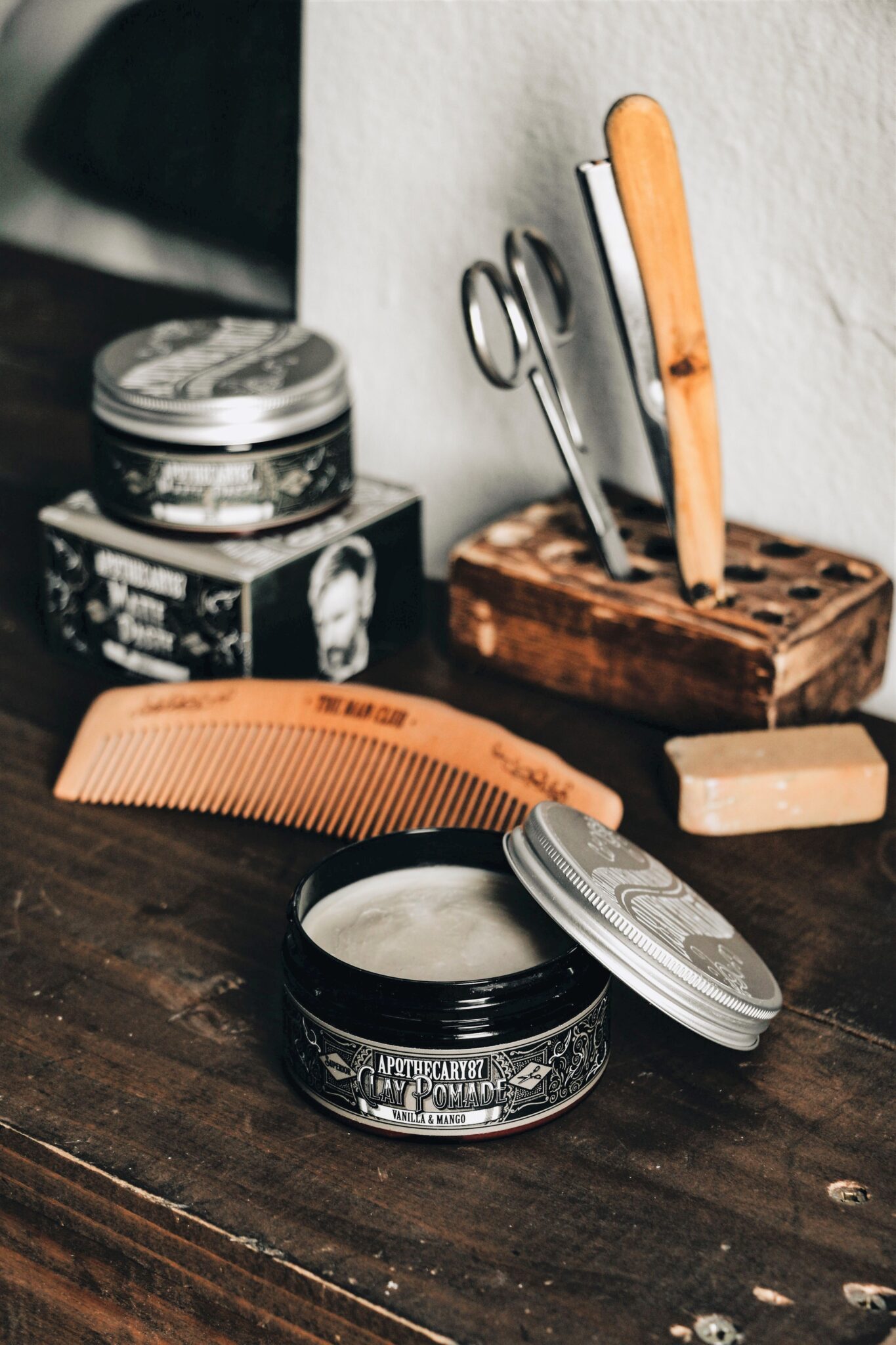 Tools of a barber are shown on a wooden table. Thera are scissors, pomade, brushes, and more. This article covers useful tips for choosing a barber. 