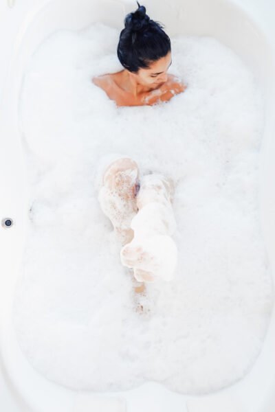 Woman smiles while she relaxes in a bathtub. This article covers why moms need guilt-free time to themselves.
