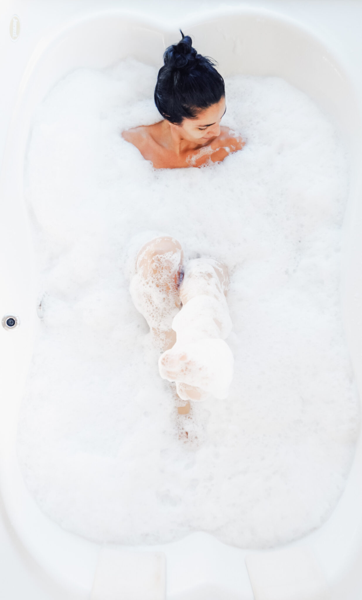 Woman smiles while she relaxes in a bathtub. This article covers why moms need guilt-free time to themselves.