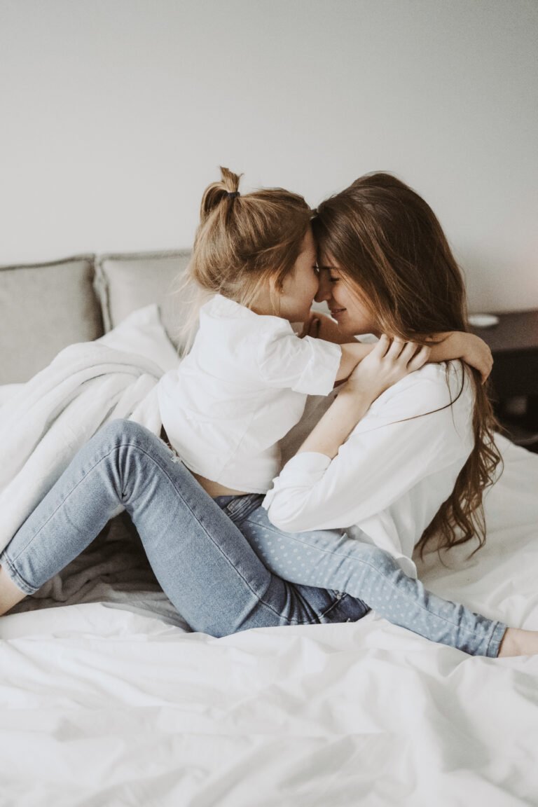 A mom and her daughter cuddle nose-to-nose on the bed. They are smiling and very happy. This article covers parenting hacks that make a world of a difference.