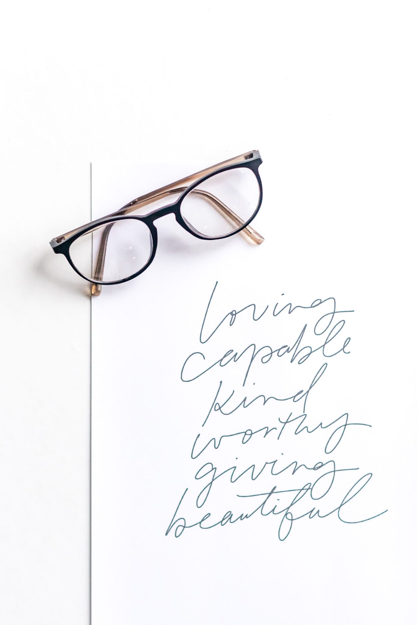 A paper shows 5 inspirational words and placed on top is a pair of black Rayban glasses. This article covers signs you might need prescription lenses.