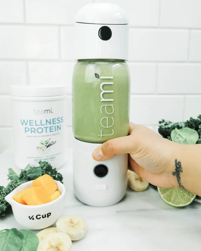 A hand presses the Teami MIXit Blender and it's surrounded by ingredients to make a green smoothie.