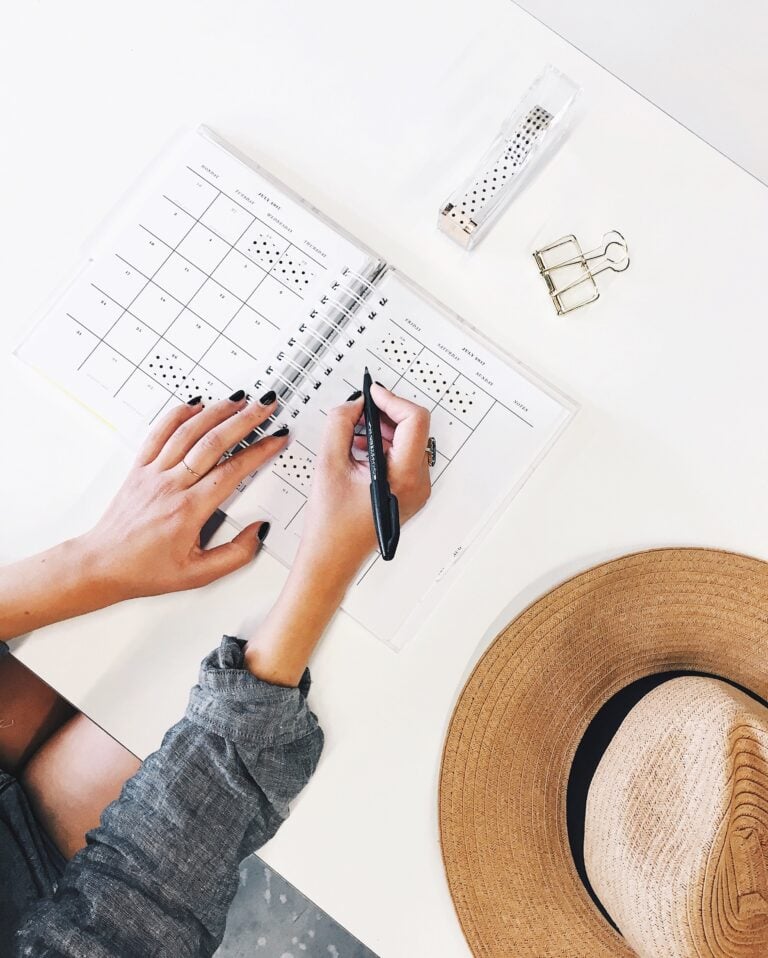 A woman writes in a planner, her hat is off and next to her. This article covers curating your home in a manner that fosters creativity.