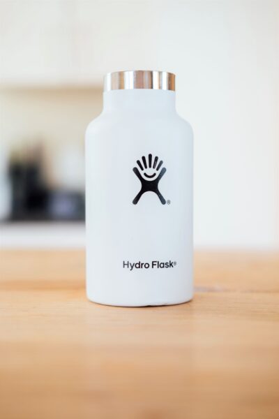 A white Hydroflask sits on a wooden table. This article covers essential back to school items that will get your kids excited for