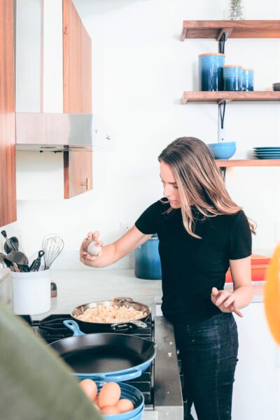 Woman seasons her food while she cooks at home. This article covers brilliant ways to cut costs and save money at home.