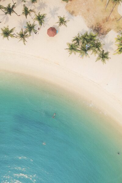 A bird's eye view of a beach, there is a person floating in the water. This article covers reasons to book a long-term holiday.