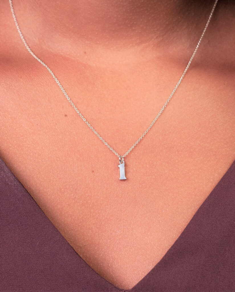 A woman wears an enneagram necklace bearing the number 1 in silver. 