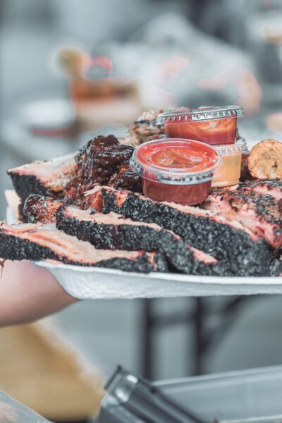 A chef holds up a large plate of Texas BBQ. It includes brisket, ribs, sausage, and pork.
