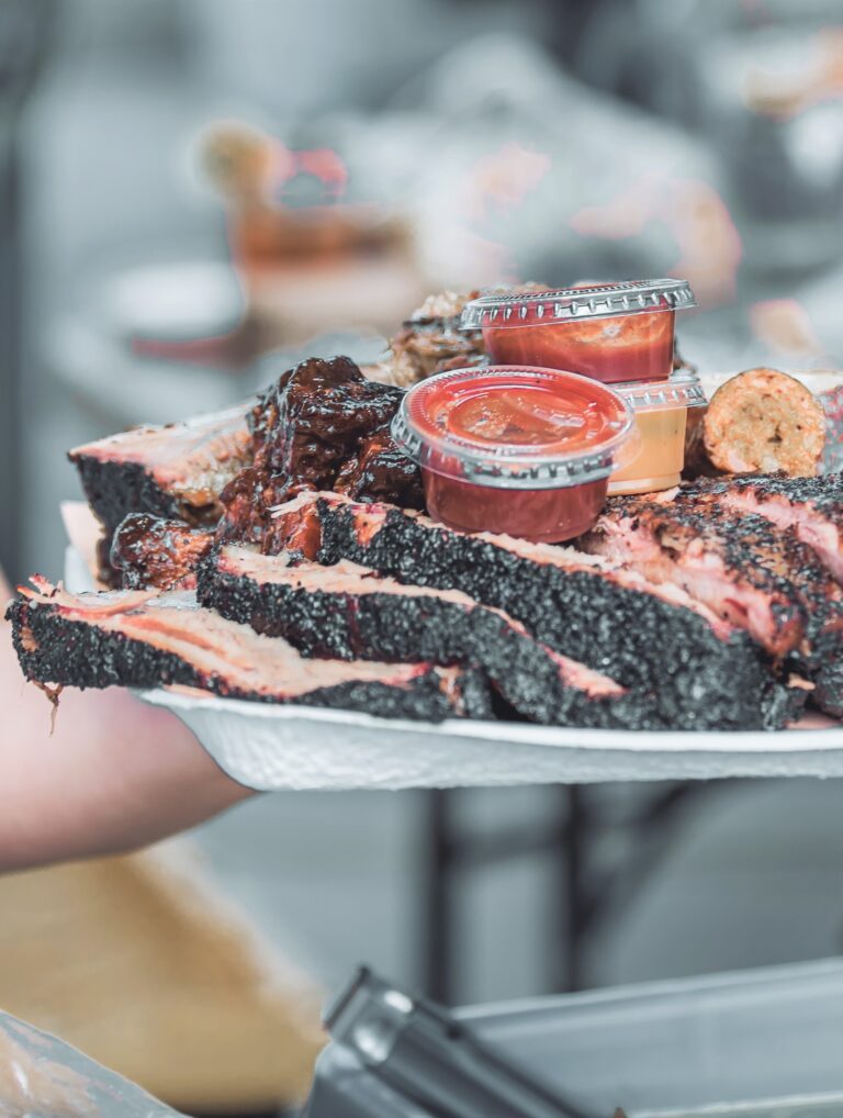 A chef holds up a large plate of Texas BBQ. It includes brisket, ribs, sausage, and pork.