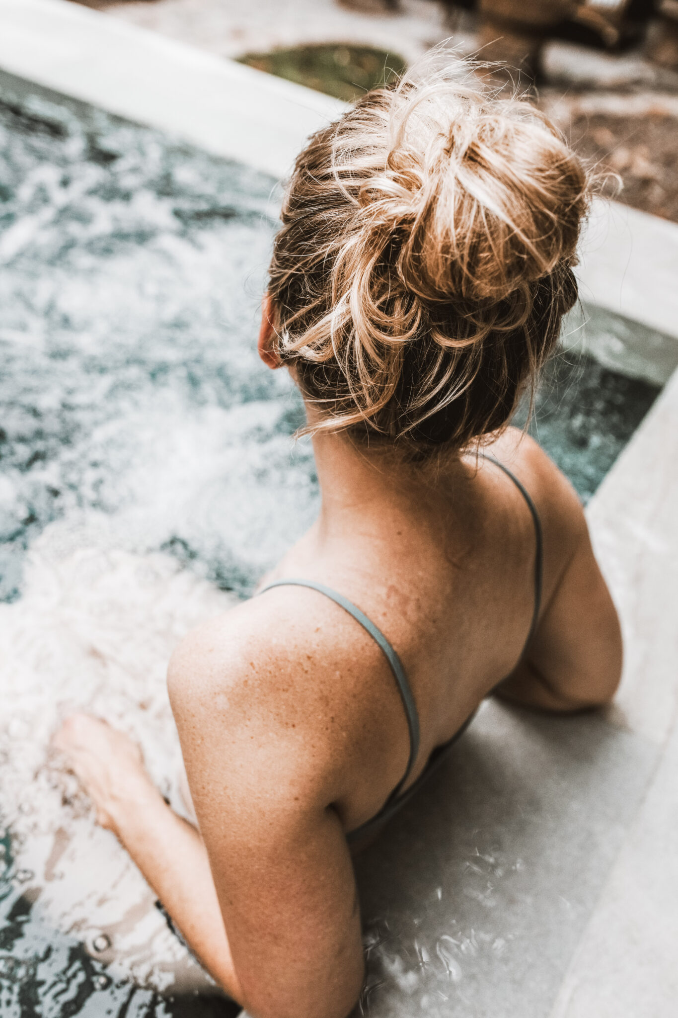 Woman is facing away from the camera and is enjoying a dip in a hot tub. This article covers why you should treat yourself to a trip to a wellness spa.