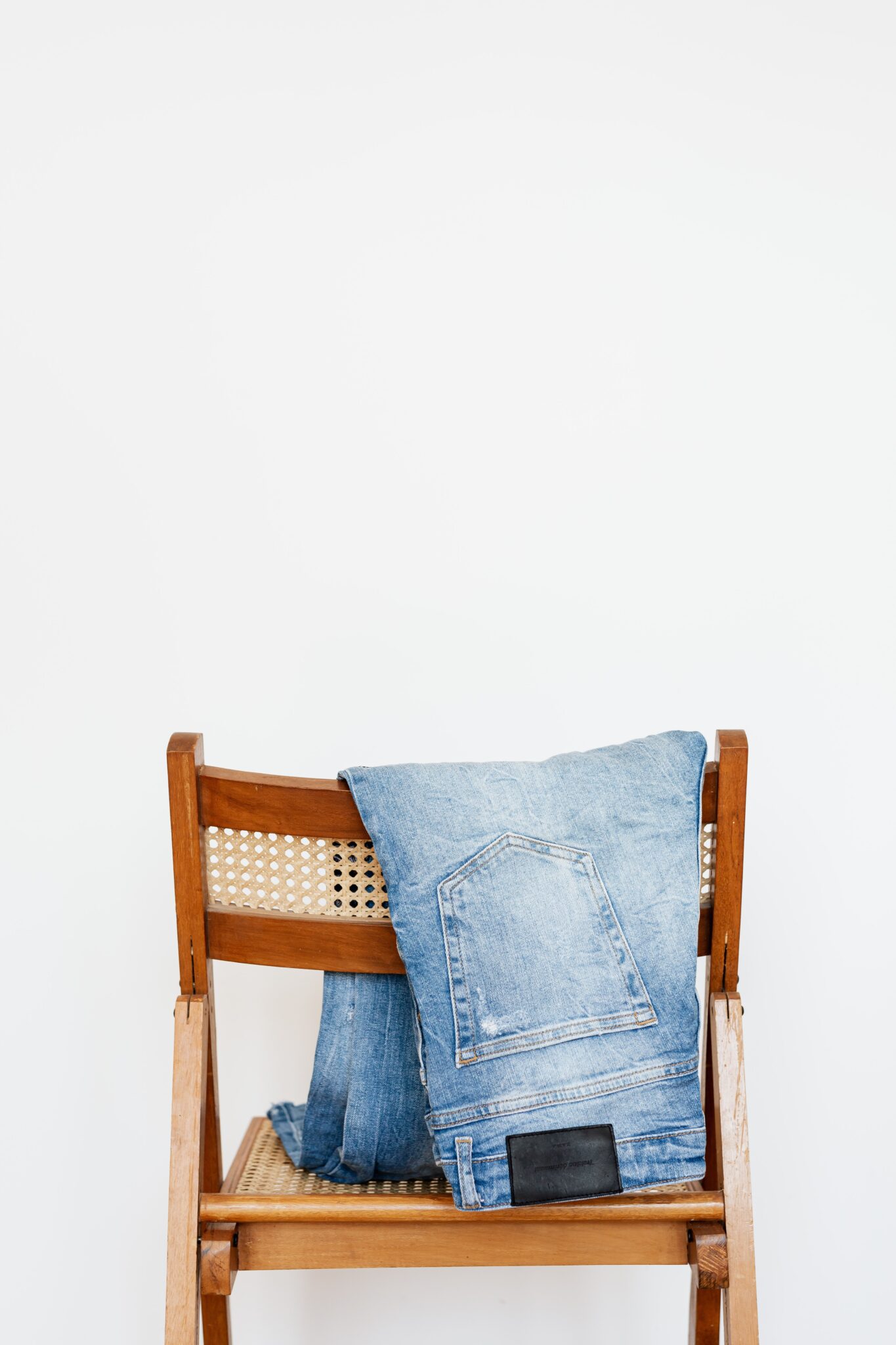A pair of jeans hangs over a wooden chair. This article covers 4 things you should know if you plan to start a clothing business.